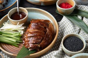 side view of traditional asian food peking duck with cucumbers and sauce on a plate