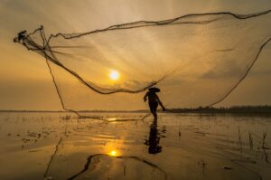 Silhouette of asia traditional fisherman in action when fishing at sunrise